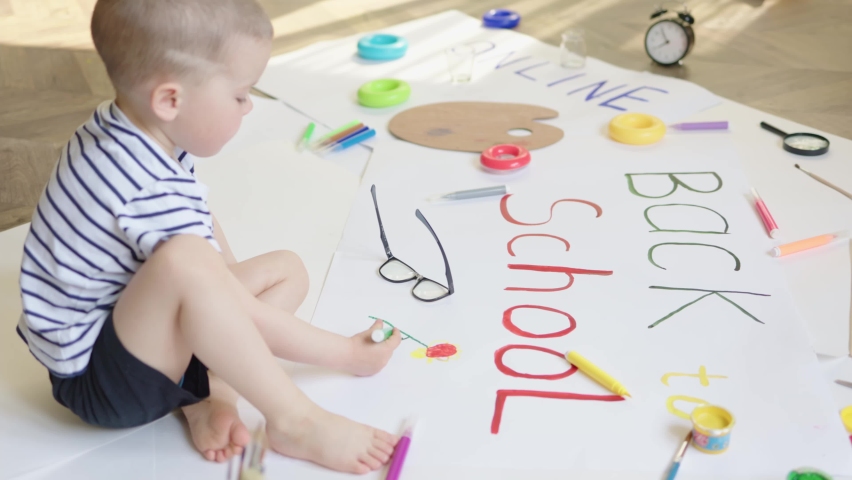 little baby child kid sitting on floor lookin at art work picture, drawn himself. preparing to school days concept. first time kindergarten starting beginning new educational year concept