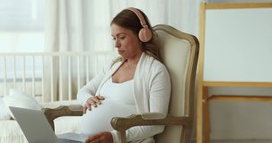 Pregnant woman in headphones sits in armchair using laptop having video call conversation to family, talk to obstetrician-gynecologist, receive professional medical on-line consultation, prenatal