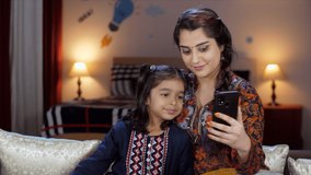An Indian housewife and her sweet daughter watching an online video on a mobile - fun and entertainment, screen addition, kids' habit . A pretty Indian mother and her little kid are using a smartph...