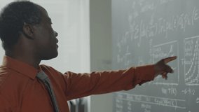 Panning shot of African American professor explaining formulas on chalkboard while diverse students listening to him during algebra lesson - Powered by Shutterstock - Get 15% off with code: PIKWIZARD15