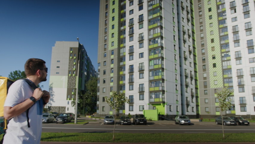 A foot courier with a yellow bag is walking down the street in search of the right building