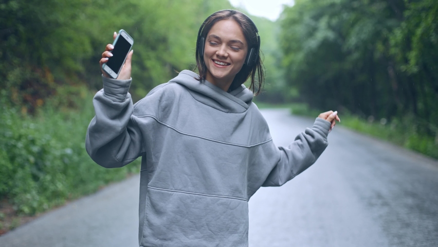 Pretty beautiful young woman girl lady blue-eyed brown-haired woman walking on the forest road alone and listening to music in headphones, happy dancing in the rain, looking around, enjoying life | Shutterstock HD Video #1093556995