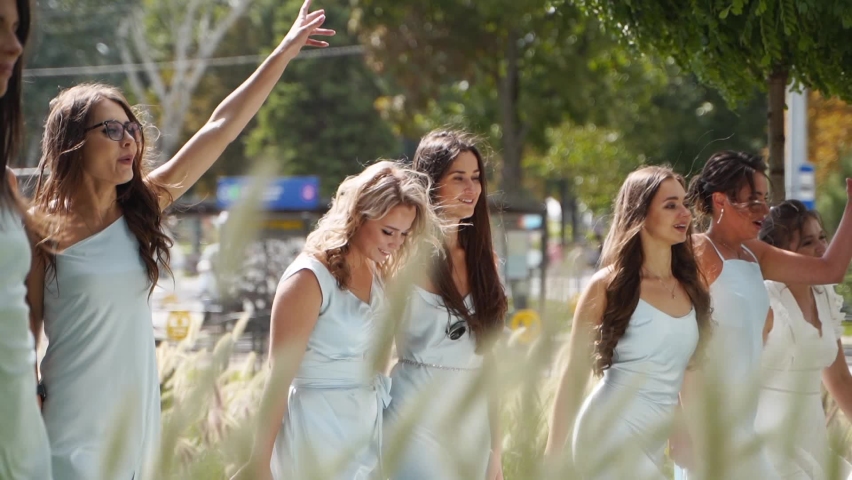 Attractive pretty bridemaids in identical pale blue dresses walk in park cheering waving hands. Women party with friends on wedding day in elegant gowns. Girlfriends on bachelorette party. Slow