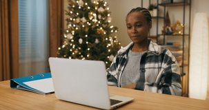 An African-looking girl sits at table in living room and has video chat. She communicates with new partners and tells them about project. The girl holds piece of paper and explains all the details.