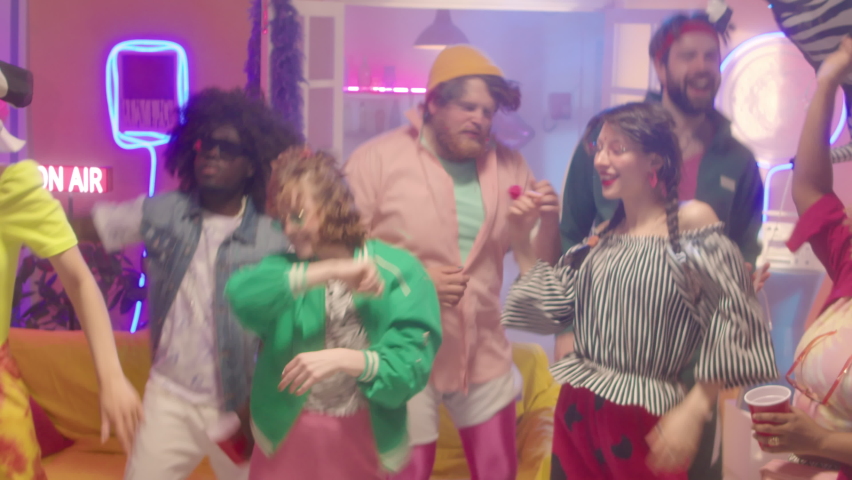 Company of young excited friends in bright trendy outfits dancing energetically together at 90s disco party in room with colorful neon light | Shutterstock HD Video #1093563063