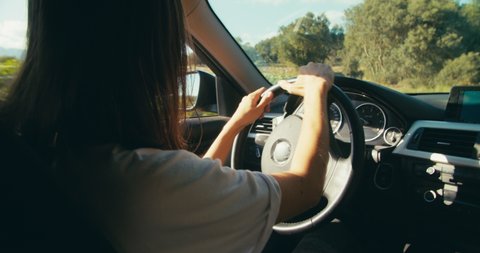 Handheld slow motion medium shot of traveler female driving car on road trip to mountain forest. Young adult brunette woman back view drive vehicle on country road.  Vídeo Stock