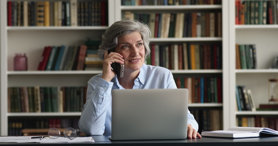 Confident happy mature senior business woman speaking on mobile phone at workplace, negotiating to partners, giving consultation, talking to customer, sitting in office, working at laptop Royalty-Free Stock Footage #1093573493