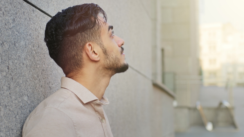 Close up side view pensive dreaming inspired bearded Hispanic Indian adult 30s businessman relaxed outdoors man resting take break standing leaning wall in city looking up in sky dream contemplating Royalty-Free Stock Footage #1093573719