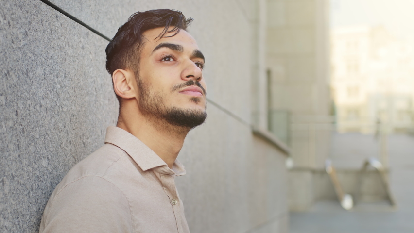 Close up side view pensive dreaming inspired bearded Hispanic Indian adult 30s businessman relaxed outdoors man resting take break standing leaning wall in city looking up in sky dream contemplating | Shutterstock HD Video #1093573719