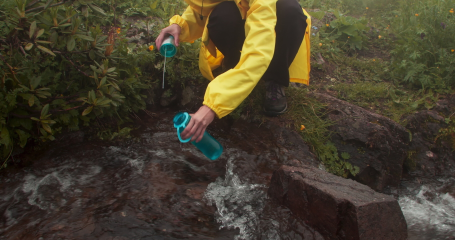 Female hiker with backpack fills bottle with clear mountain stream water. Woman drinking clear mountain water | Shutterstock HD Video #1093578183