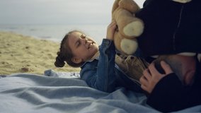 Small kid play parents on sea beach. Happy family spend time together at seashore. Cute little girl holding teddy bear on nature outside close up. Playful people enjoy summer vacation. Holiday - Powered by Shutterstock - Get 15% off with code: PIKWIZARD15