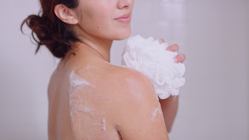 Woman washes shoulder with body wash suds with happy relaxed expression