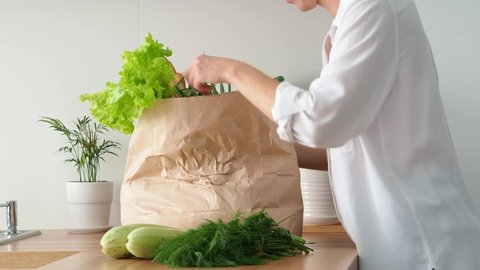 A woman put a bag of groceries on the kitchen table. Women's hands put greens and vegetables on the table. Bring groceries from the store. Eco-friendly paper packaging., videoclip de stoc