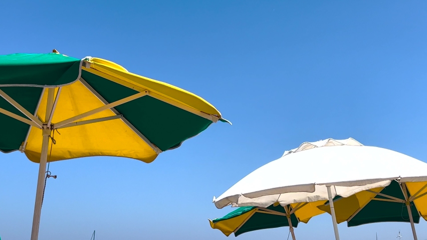 Group of striped beach umbrellas against blue sky at swimming pool. Sunny perfect chilling day. Covering the sun parasols creating a nice shadow for relaxation. Summer vacations 4k background  Royalty-Free Stock Footage #1093586171