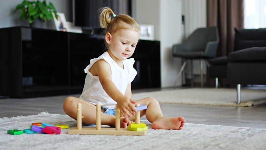 Cute caucasian little girl playing on the floor at home with eco wooden toys. Montessori toy. The child playing educational games. High quality 4k footage