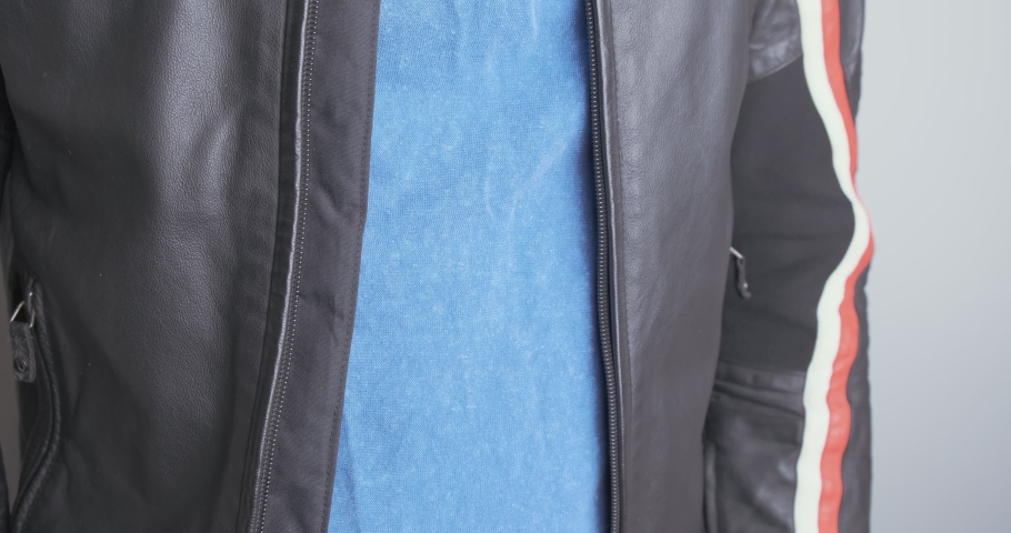 Man zips up a black leather jacket. Close-up, chest, front view.