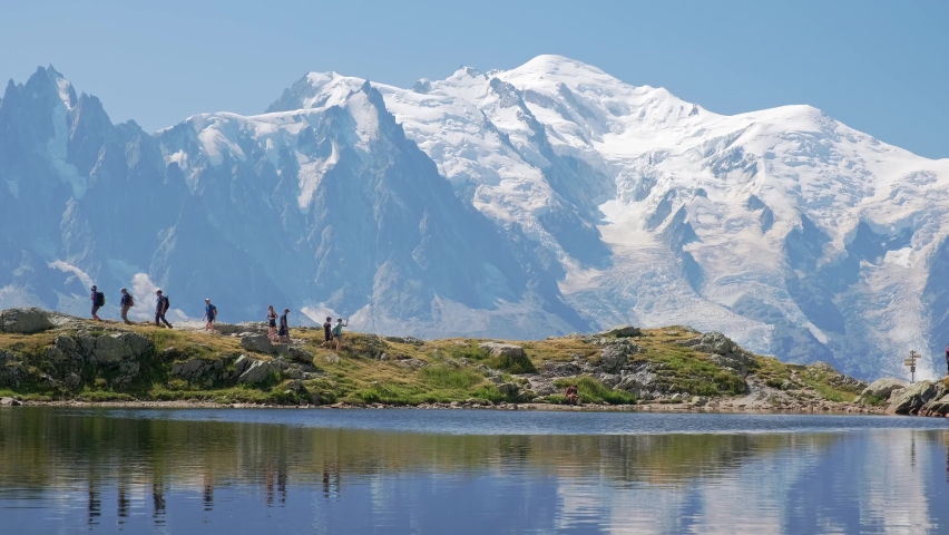 people hiking with reflections of the mountains, and behind the view of the mont blanc, in the valley of chamonix, in france in a sunny day. Static shoot.