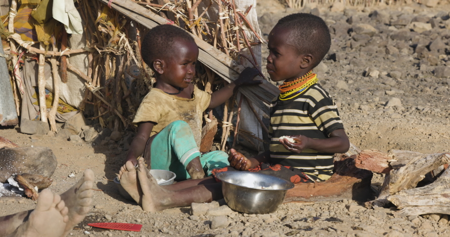 Close-up.Malnourished children due to extreme poverty, drought and climate change. Eating maize porridge infront of their dwelling.Kenya Royalty-Free Stock Footage #1093592765