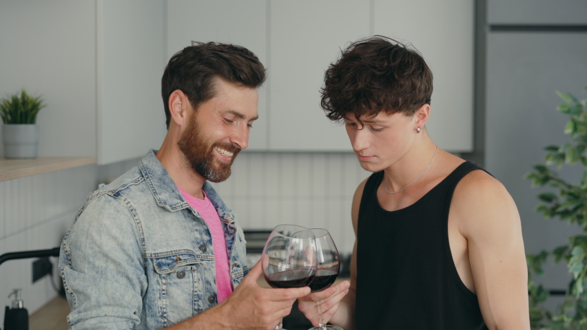 Lgbt couple standing in their new apartment drinking wine from the glasses feeling happy and in love together. Romantic evening. People relationships concept
