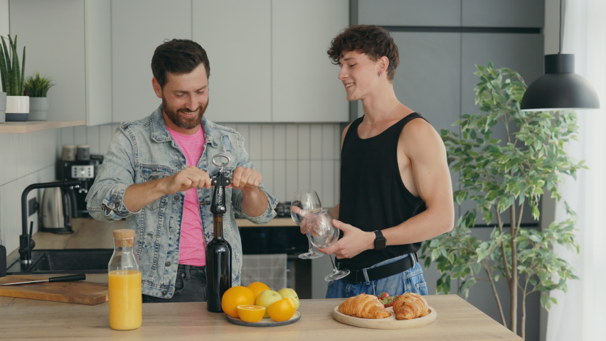 LGBT male couple in love preparing a romantic dinner and one of the partners opens the wine while another holding two glasses. People relationship and pride freedom concept