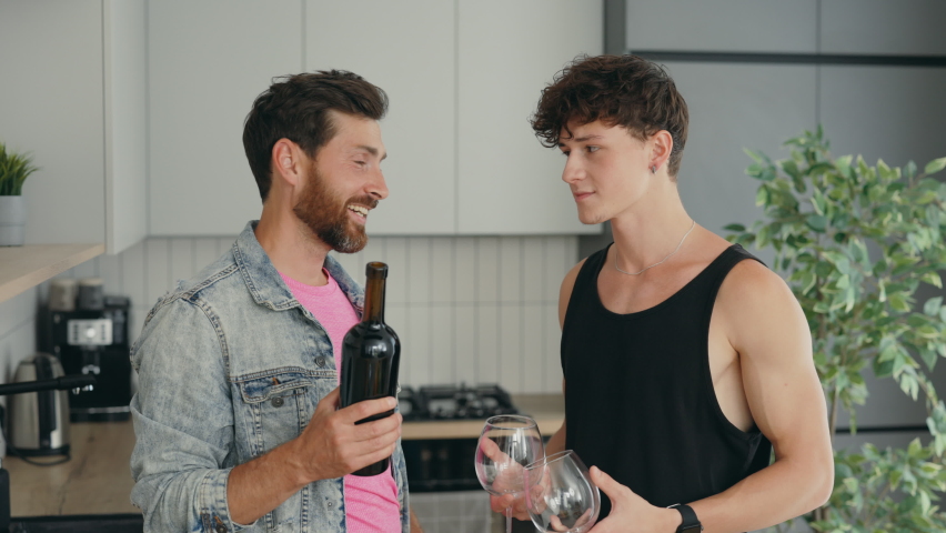 Lgbt gays couple standing at home one partner holding the bottle of wine and another holding two glasses before the romantic dinner. People relationships concept