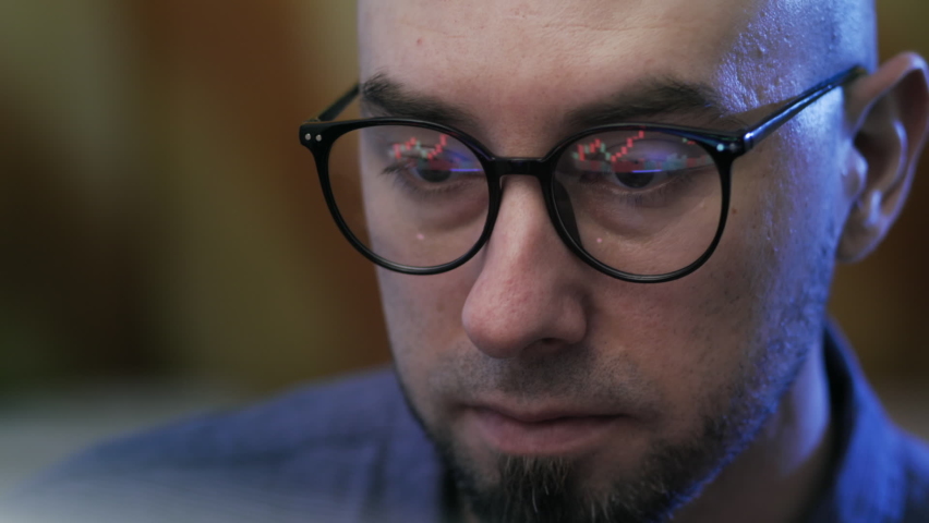 Portrait of bald focused man trader wearing eyeglasses looking at a computer screen with trading charts reflected in glasses. Concept of stock trading market, analyst and cryptocurrency. Royalty-Free Stock Footage #1093595295