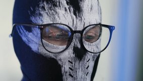 Close-up of face of an unknown person in a balaclava and glasses looks attentively at computer monitor with a trading platform. Reflections in lenses of trader. The concept of cybercrime. - Powered by Shutterstock - Get 15% off with code: PIKWIZARD15