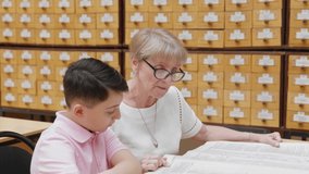 4K. A happy elderly grandmother listens to a little school-age boy reading a book in the library. - Powered by Shutterstock - Get 15% off with code: PIKWIZARD15