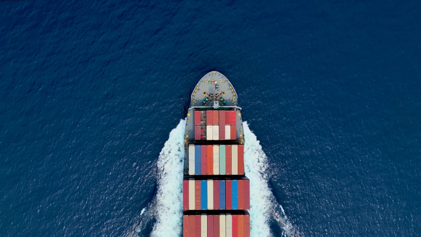 Aerial top down view of a bow from a large container cargo ship traveling with speed over blue ocean