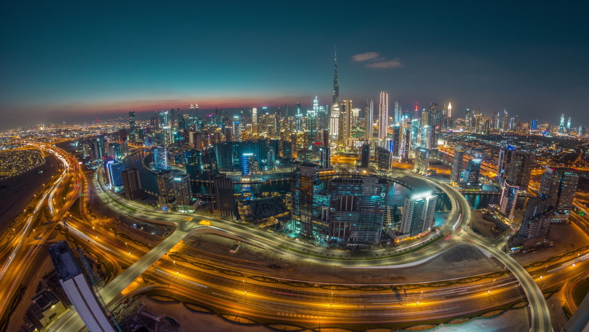 Panoramic skyline of Dubai with business bay and downtown district day to night timelapse. Aerial wide angle view of many modern skyscrapers with traffic on al khail road after sunset.