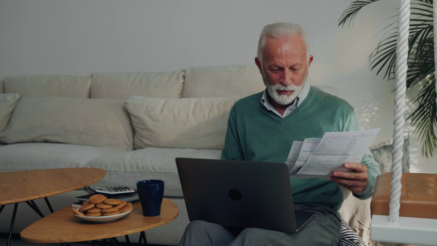 A worried elderly caucasian man is lookin at his monthly bills and is very upset about them.
