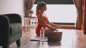 Portrait of blonde beautiful woman doing yoga and relaxing her mind and her body at home on the floor. One active and heathy girl taking care of health training. Following a video tutorial on laptop 
