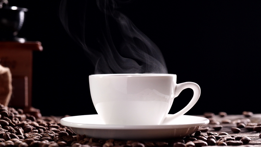 Hot Coffee Cup Concept. Close-up white coffee cup, mug with beautiful steaming smoke, classic vintage coffee grinder espresso manual, beans, burlap on on old wooden table dark, black backgrounds | Shutterstock HD Video #1093602645