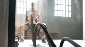 Video of athletic fitness man training with black battle ropes at gym.