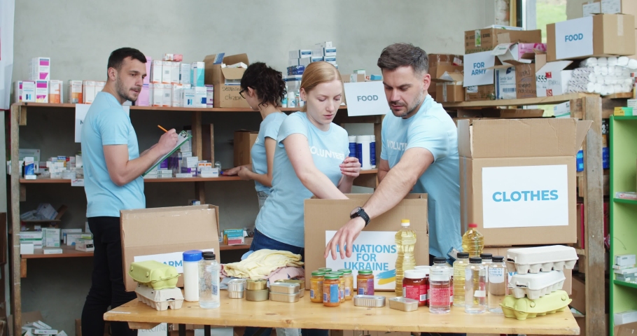 One couple of caucasian volunteers packing and sorting donated food while another pair doing inventory on shelves. Concept of teamwork, charity organization and sincere help. Royalty-Free Stock Footage #1093605911
