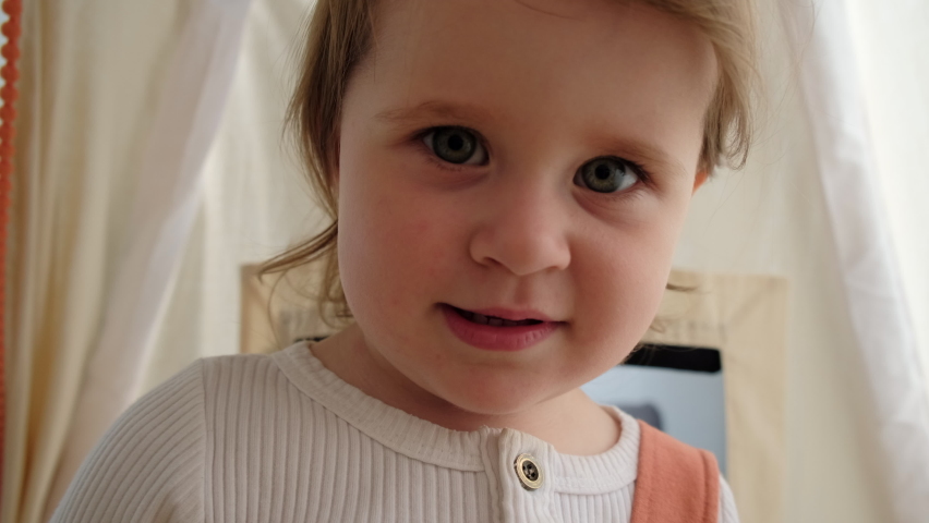 Selective focus of little girl child standing in cozy tent looking at camera waving hello greeting, webcam view baby preschool kid daughter doing hi goodbye gesture with hand, video conference concept