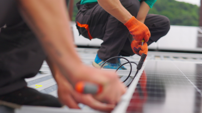 Installation, Connection and mounting of solar panels. Two workers fasten solar panels. Technicians installing solar panels on metal stand. Workers installing PV solar panels on the roof of a house. Royalty-Free Stock Footage #1093608575