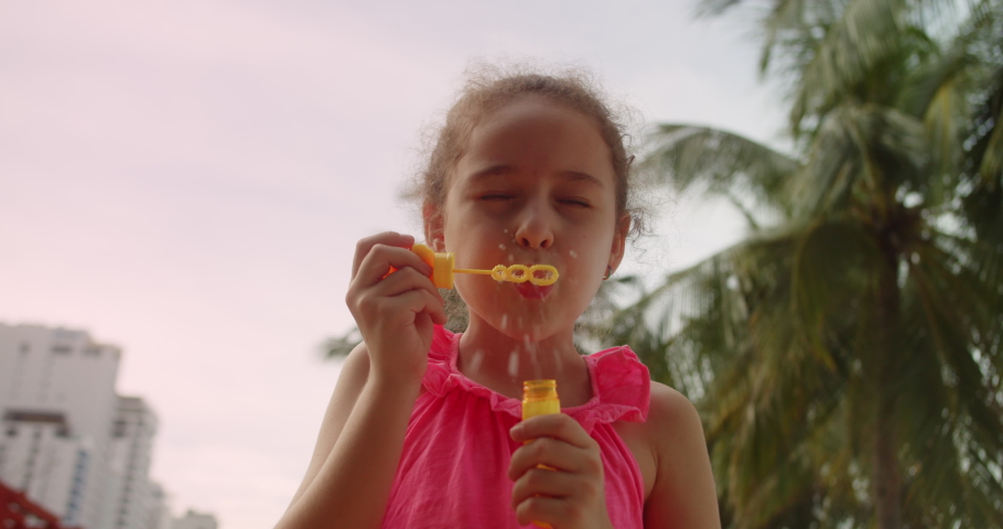 Beautiful happy shot cute and adorable little girl child is blowing soap water bubbles against the sun in the park.Funny happy little girl smiling child adorable looking at camera is play on Beach.