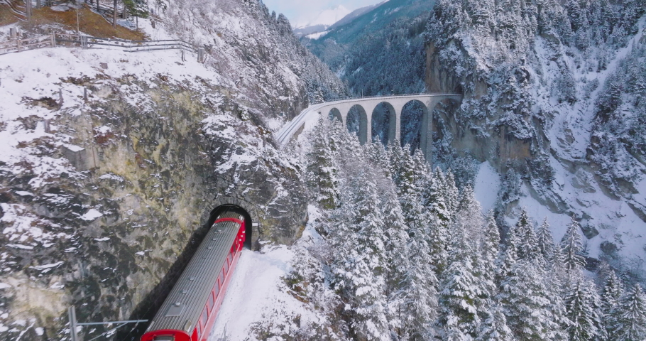 Landwasser Viaduct world heritage sight with luxury Glacier and Bernina express in Swiss Alps snow winter scenery. Aerial Drone shot red train passing through famous mountain in Filisur, Switzerland. Royalty-Free Stock Footage #1093618615