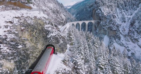 Landwasser Viaduct world heritage sight with luxury Glacier and Bernina express in Swiss Alps snow winter scenery. Aerial Drone shot red train passing through famous mountain in Filisur, Switzerland. Video Stok