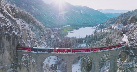 Landwasser Viaduct world heritage sight with luxury Glacier and Bernina express in Swiss Alps snow winter scenery. Aerial Drone shot red train passing through famous mountain in Filisur, Switzerland.: stockvideo