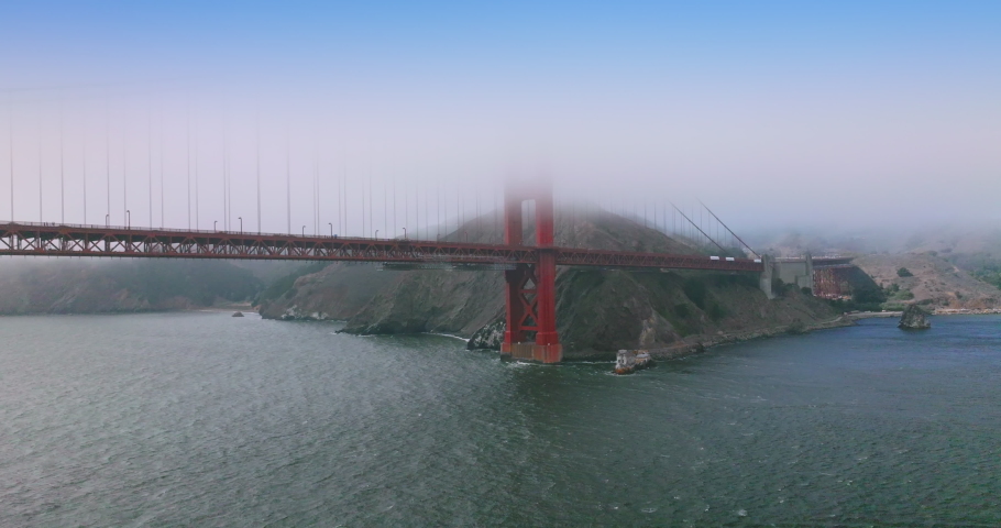 Part of beautiful famous Golden Gate Bridge at the backdrop of rocks. Hills and bridge tops hiding in the thick fog of San Francisco.