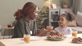 Waist up slowmo of happy African American military woman and her cute little daughter feeding each other with homemade sandwiches, sitting at kitchen table in cozy home - Powered by Shutterstock - Get 15% off with code: PIKWIZARD15
