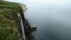 A tall waterfall runs straight to the ocean from the cliff, in a foggy atmospheric morning. a 4K video clip. Kilt Rock and Mealt Falls, Isle of Skye, Scotland.