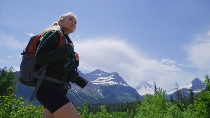 Close-up view of a female traveler hiking along tourist trails in Glacier National Park. Woman exploring pristine wilderness with rocky mountainous range in the background. High quality 4k footage