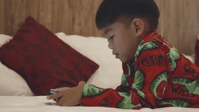 Kid watching videos and cartoons online in bedroom at home, Little Asian boy playing digital tablet on bed addicted game and cartoon, internet funny online concept