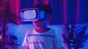 Asian little kid boy wearing virtual reality goggles experiencing reality, Child wear VR helmet look left look right and excited at home dark purple and blue background, Virtual technology