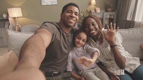 Handheld POV slowmo of delighted African American soldier smiling at camera while taking selfie with his beloved wife and pretty little daughter, sitting together on soft grey couch in living room - Powered by Shutterstock - Get 15% off with code: PIKWIZARD15