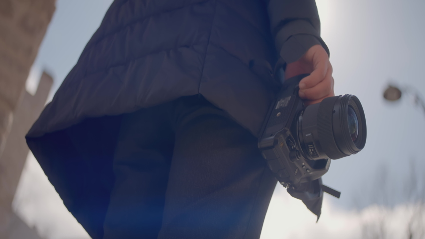 Close-up of photographer holding professional camera. Action. Camera is in hands of professional young photographer. Woman takes pictures on camera