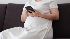 A video of a pregnant woman holding a smartphone and operating it while sitting on a sofa